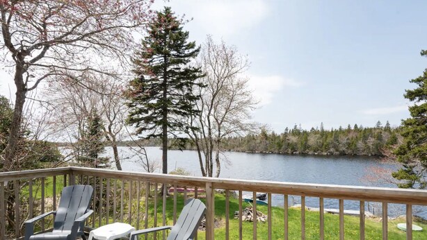 A deck with two Adirondack chairs and a small table, overlooking a lake with trees and a grassy area. - Private Lakefront Escape – Swim, Sip Wine & Stargaze – 25 Mins to Halifax (Brookside)