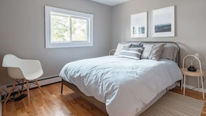 A bedroom with a bed, a chair, a window, and two framed pictures on the wall. - Private Lakefront Escape – Swim, Sip Wine & Stargaze – 25 Mins to Halifax (Brookside)