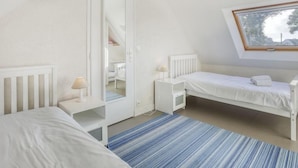 Ein Schlafzimmer mit schrägen Wänden, einem Fenster, einem Kleiderschrank, einem Nachttisch und einem Bett.