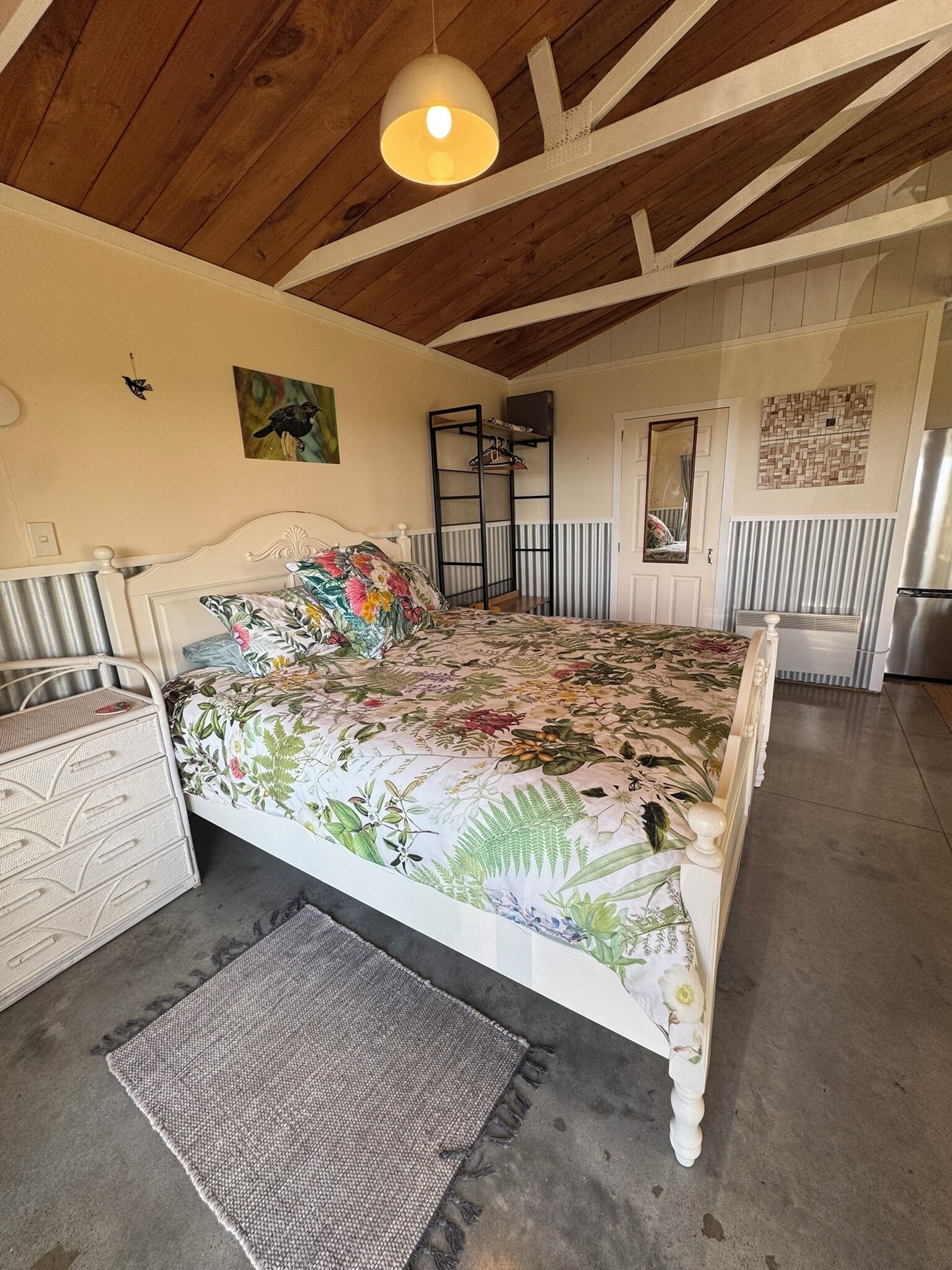 A bedroom with a bed, a dresser, a hanging light fixture, a radiator, and a mirror.