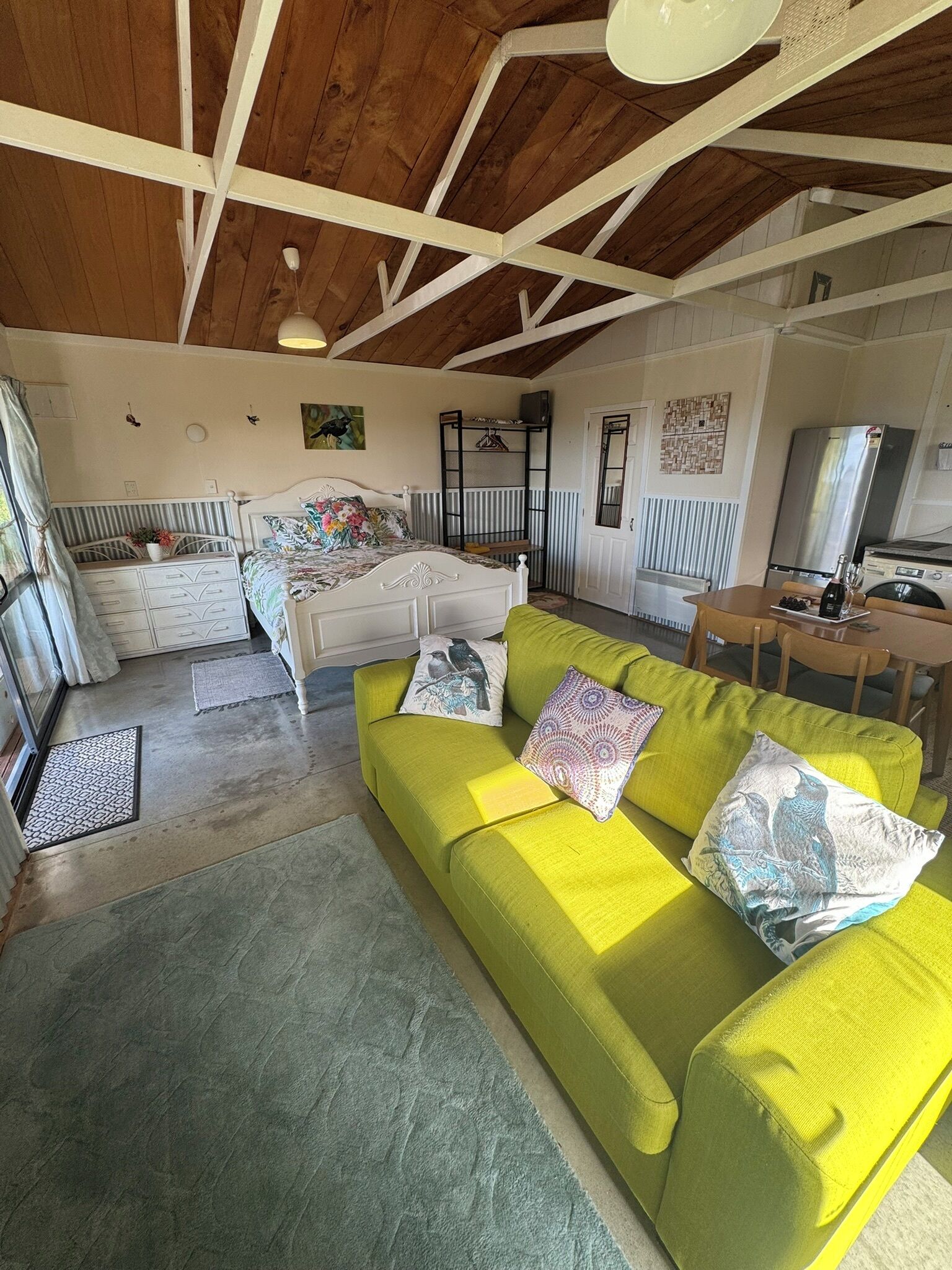 Een kamer met een bed, een groene bank, een houten plafond en een keukenhoek.