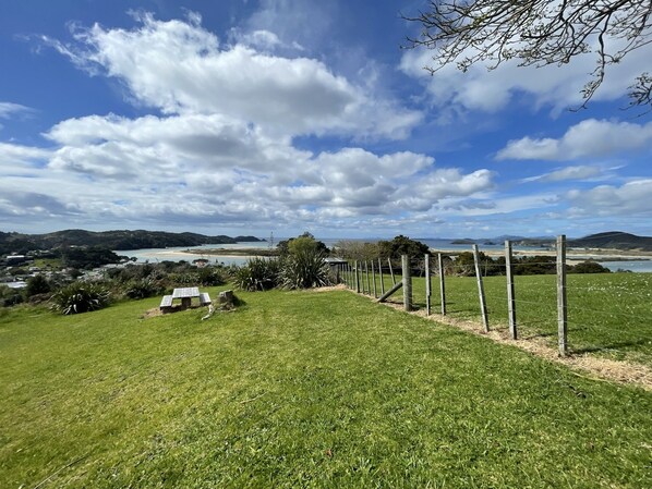 A grassy field with a wooden fence, a small wooden structure, and a scenic view of a beach and water body in the distance.