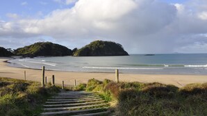 Una playa con una escalera de madera que baja a la orilla, rodeada de zonas verdes y una valla.
