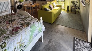 Una habitación acogedora con una cama, un sofá verde, una zona de cocina y una mesa de comedor.