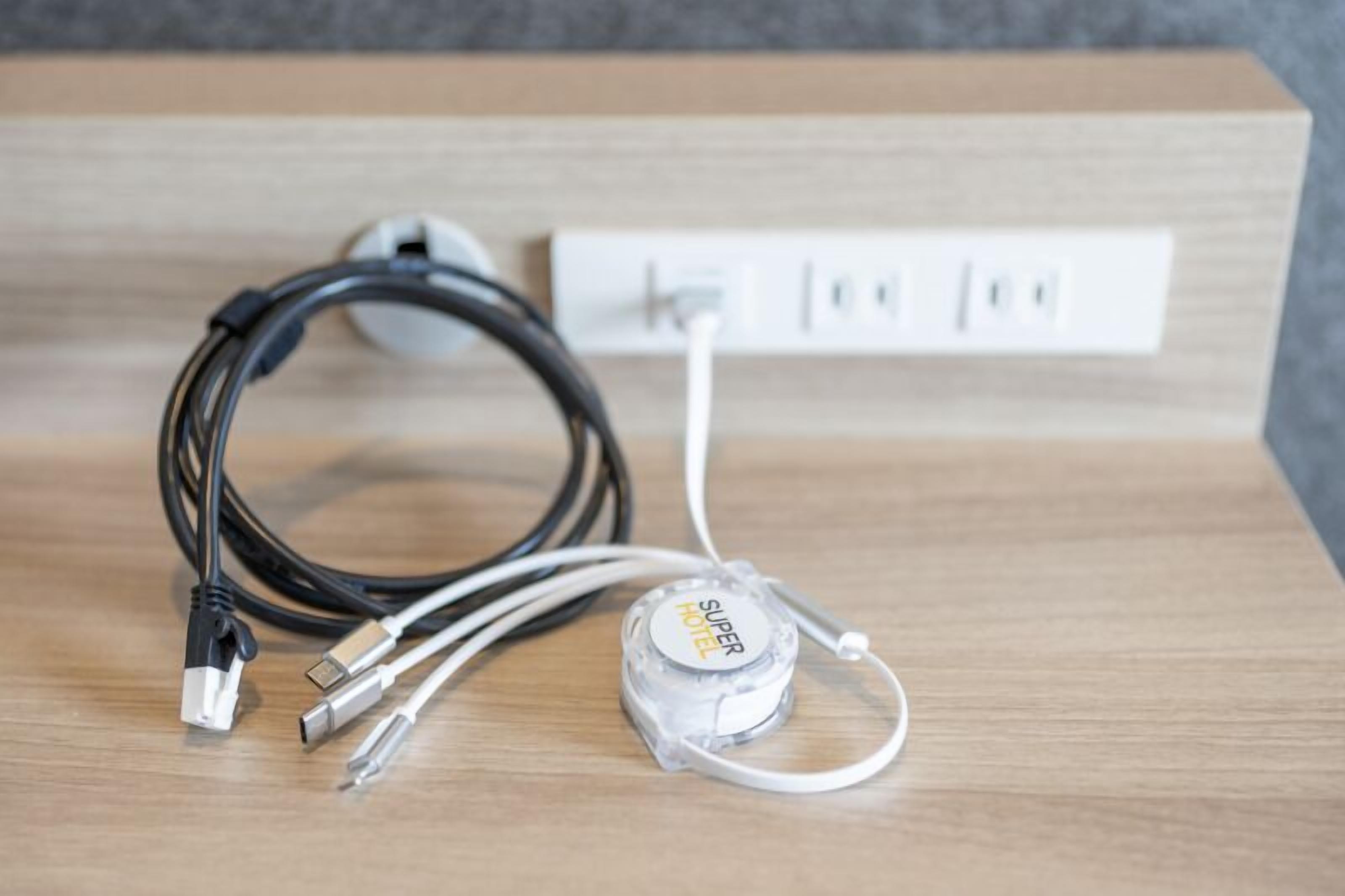 A power strip with multiple cables and a transparent surge protector labeled "SUPER HOTEL" on a wooden surface.