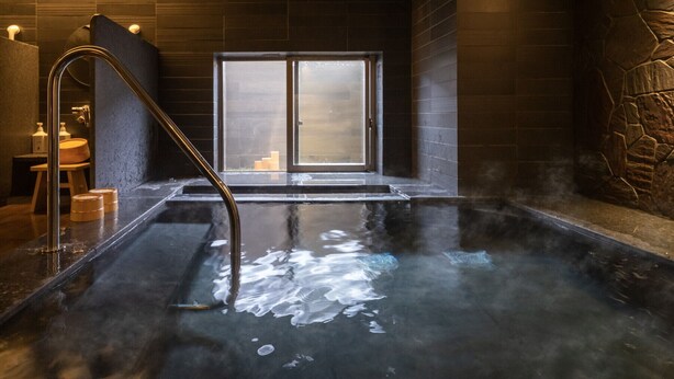 A hot spring bath with a metal ladder, wooden stools, and a stone wall. - Super Hotel Kanku Kumatoriekimae (Kumatori)