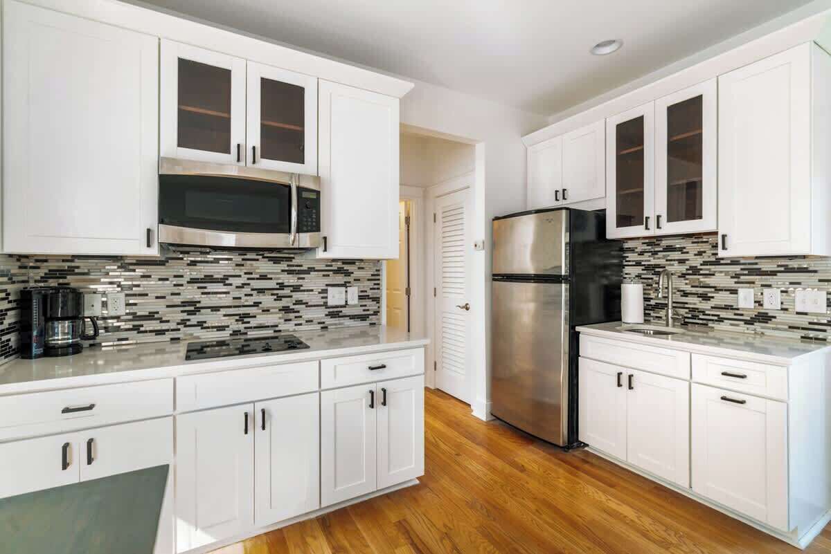 A modern kitchen with white cabinets, stainless steel appliances, and a mosaic backsplash.