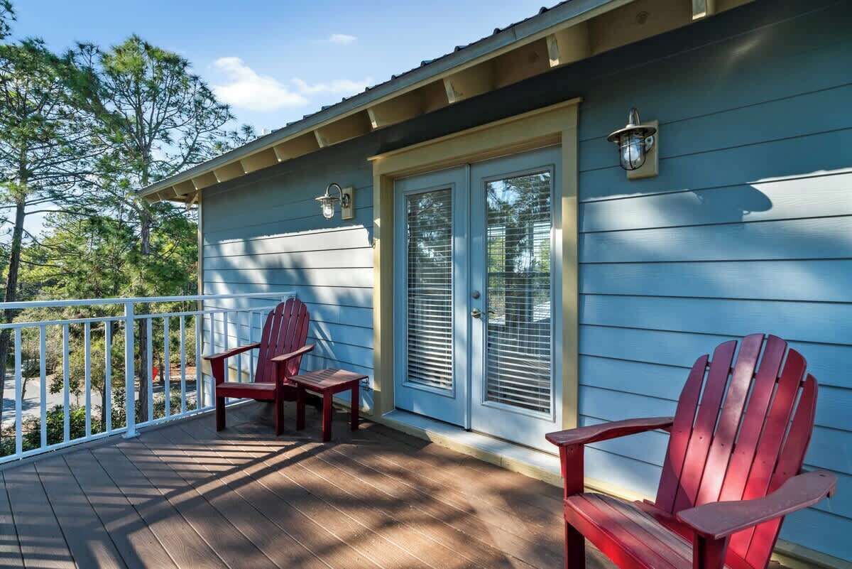 A wooden deck with two Adirondack chairs and a door with a window.