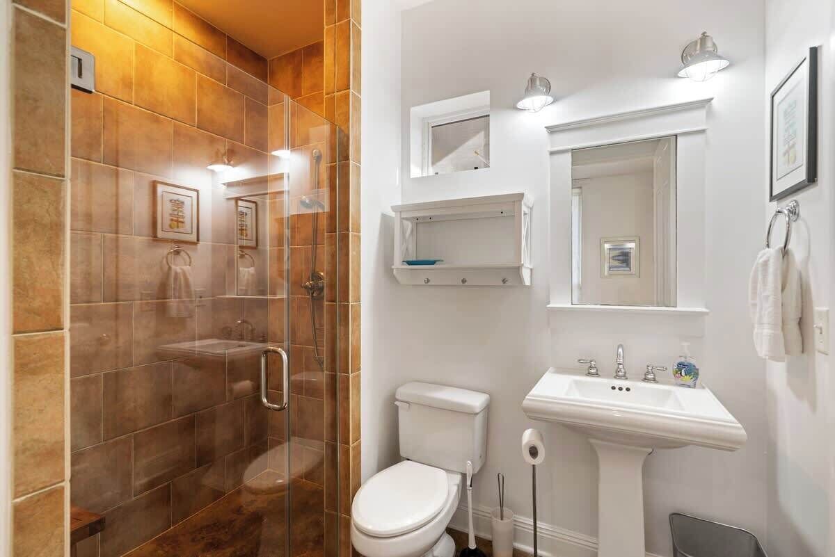 A bathroom with a glass-enclosed shower, a white toilet, a pedestal sink, and a mirror above the sink.
