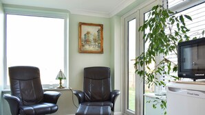 A room with two leather chairs, a painting on the wall, a television, and a plant by the window. - 3 bedroom accommodation in Ryde (Ryde)