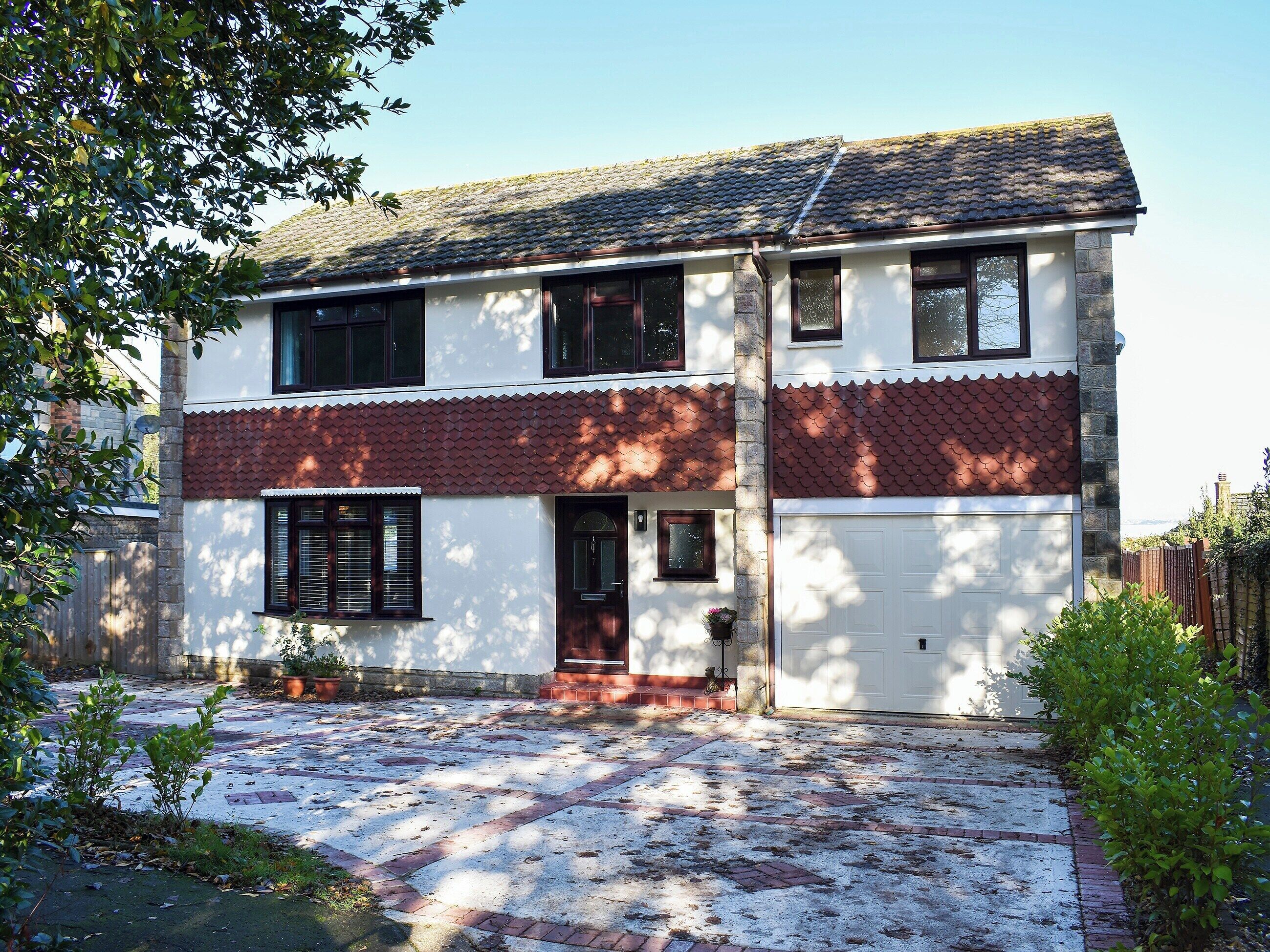 Une maison à deux étages avec un garage, un toit recouvert de tuiles et un chemin en briques menant à l’entrée.