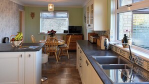 A kitchen with a dining area, wooden cabinets, a built-in oven, and a large window with blinds. - 3 bedroom accommodation in Ryde (Ryde)