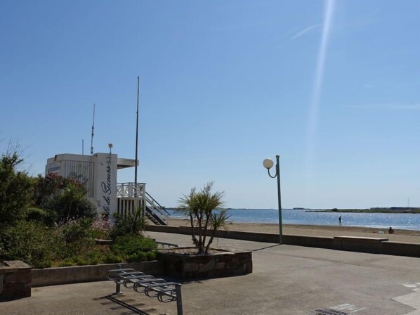 Un paseo marítimo con un edificio moderno, zonas de estar y una vista despejada al mar.