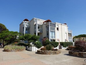 A multi-story residential building with balconies, surrounded by landscaped gardens and stone planters.