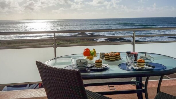 Una mesa con comida y bebidas en un balcón con vista al océano.