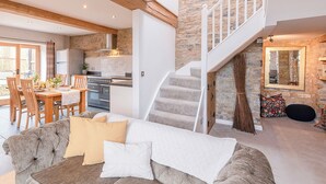 A spacious living area with a dining table, comfortable seating, a kitchen with modern appliances, a staircase, and a stone wall. - 2 bedroom accommodation in Wrantage, near Taunton (Wrantage, near Taunton)