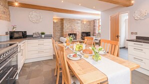 A modern kitchen with a dining area, featuring a stone wall, wooden beams, and a large dining table set for a meal. - 2 bedroom accommodation in Wrantage, near Taunton (Wrantage, near Taunton)