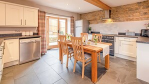 A modern kitchen with wooden beams, a dining table with chairs, a refrigerator, and a stone wall. - 2 bedroom accommodation in Wrantage, near Taunton (Wrantage, near Taunton)