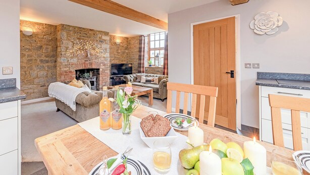 A cozy living room with a stone fireplace, a sofa, and a dining table set with food and drinks. - 2 bedroom accommodation in Wrantage, near Taunton (Wrantage, near Taunton)