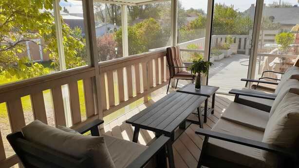 A covered outdoor seating area with wooden furniture and a view of the neighborhood.