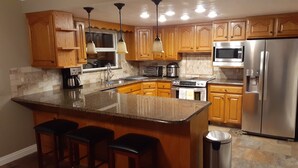 A modern kitchen with wooden cabinets, stainless steel appliances, a granite countertop, and bar stools.