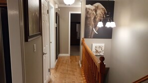 Stroll through this elegant hallway featuring a door, framed artwork, and a light fixture with three lamps.