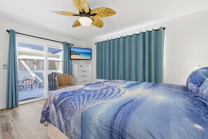 A bedroom with a bed, a ceiling fan, a TV, and a view of the outside.