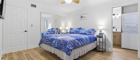 Un dormitorio con cama, ventilador de techo, espejo, pared con cita motivacional y zona de lavandería.