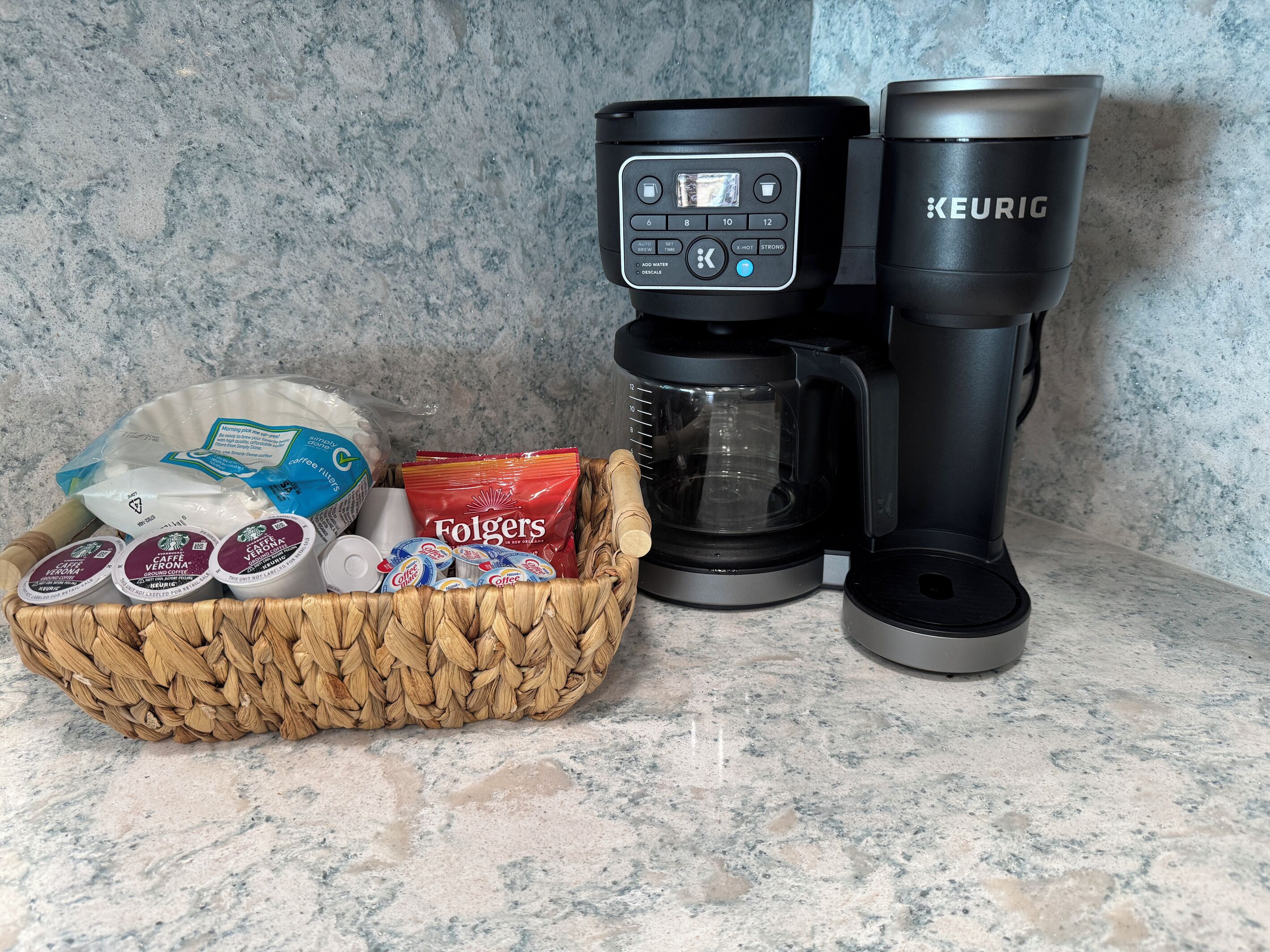 A coffee maker, a Keurig, and a basket of coffee pods and Folgers coffee bags on a countertop.