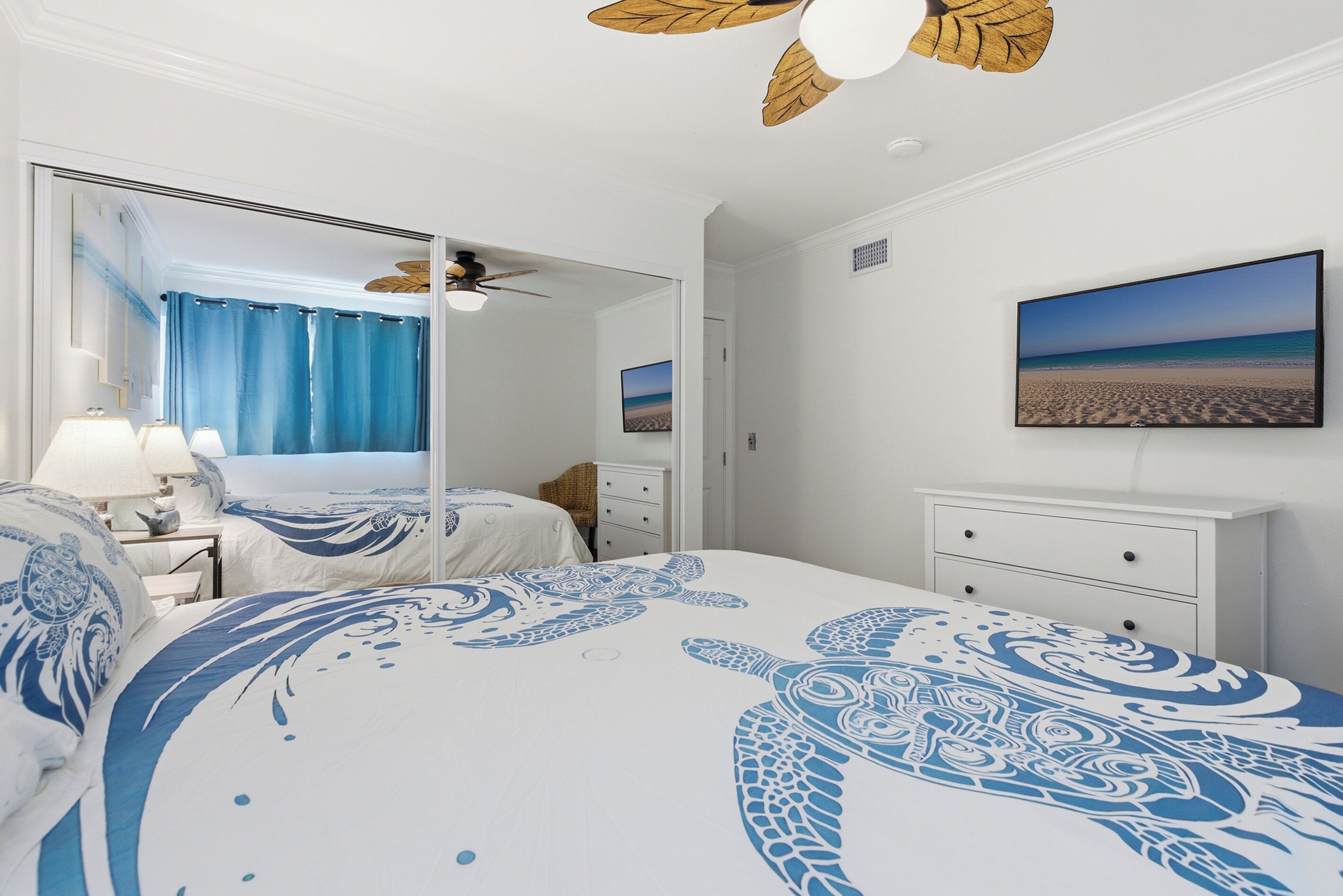 Quarto com cama grande, ventilador de teto, televisão e vista para a praia.