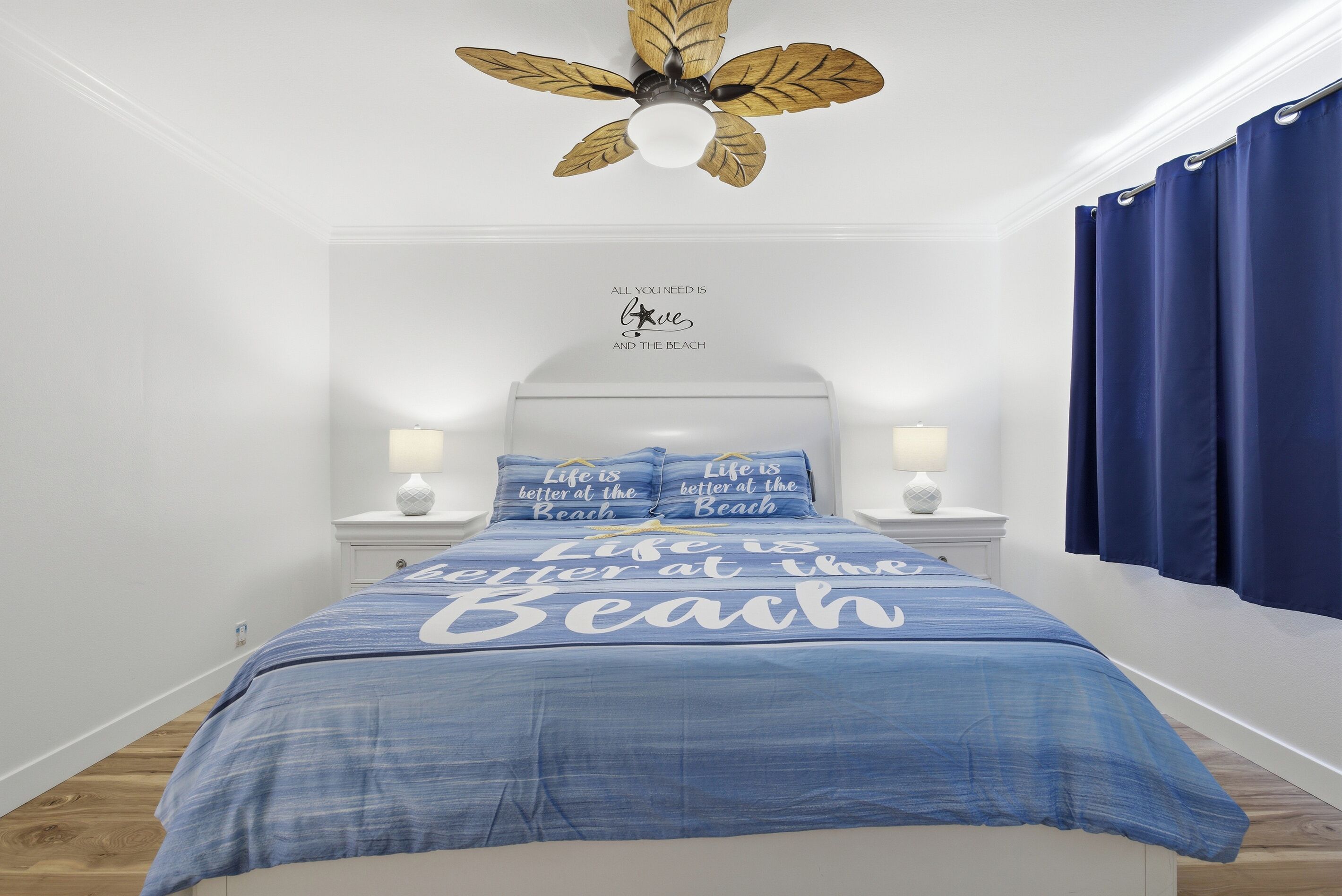 Un dormitorio con cama, ventilador de techo, una pared con una cita y una ventana con cortinas.