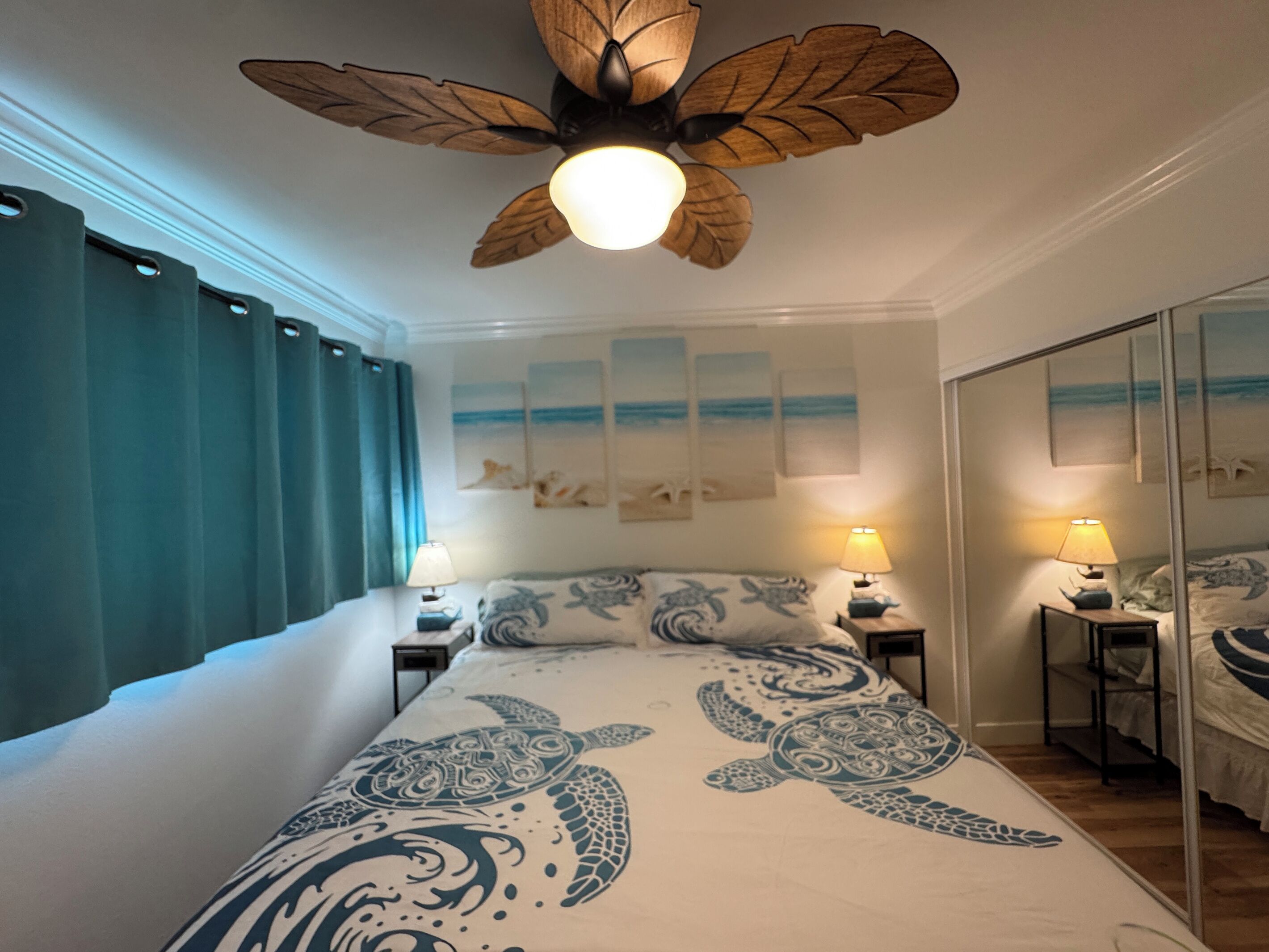 Een slaapkamer met een bed, twee nachtkastjes met lampen, een plafondventilator en een grote spiegel.