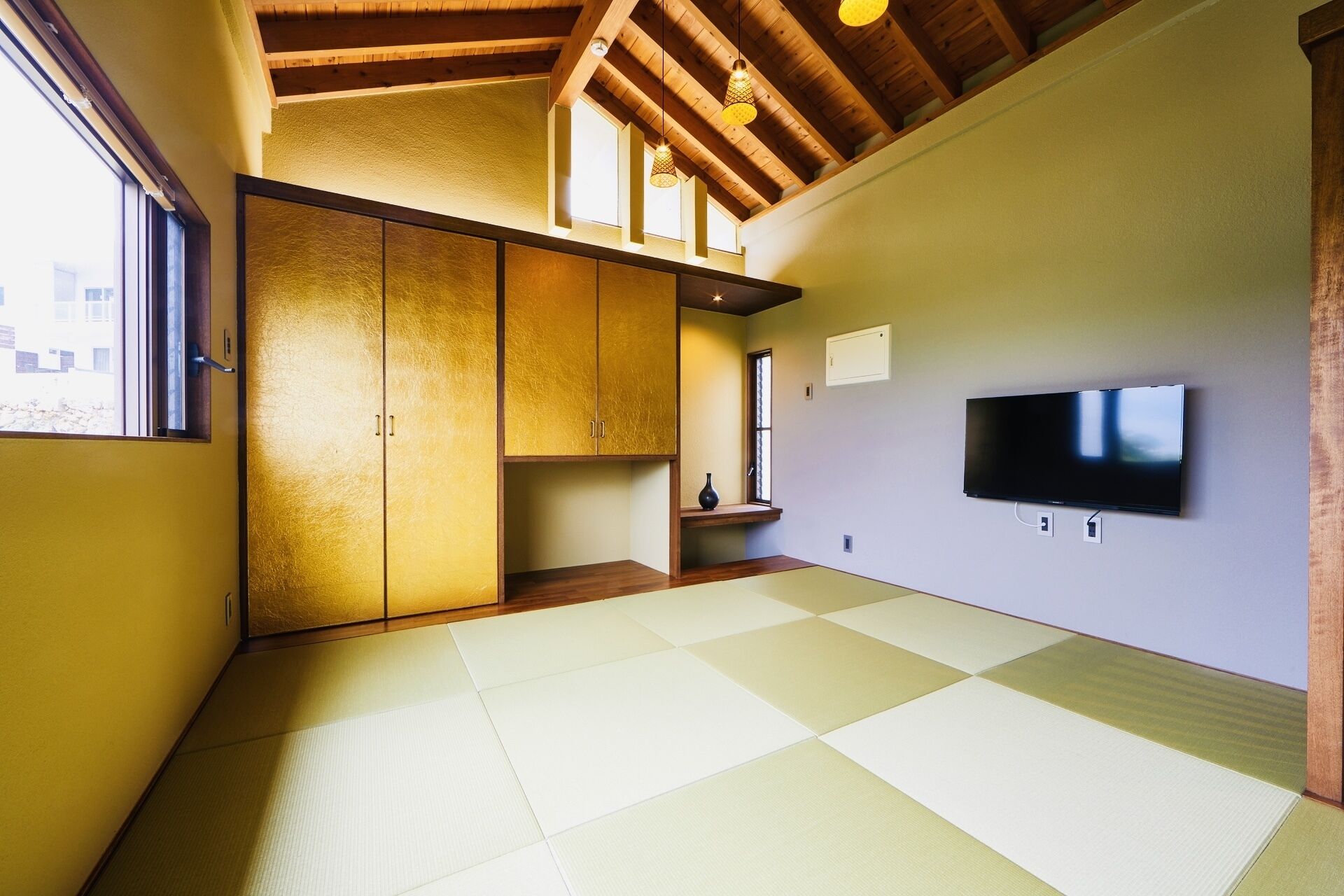 Ein Zimmer mit Tatami-Böden, Holzschränken, einem an der Wand befestigten Fernseher und einem Fenster mit Tageslicht.