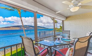 Varanda com mesa posta para refeições, com vista para uma praia com palmeiras e o oceano.
