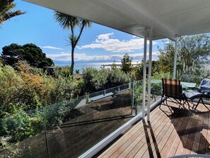 A balcony with a glass railing overlooking a garden and a view of the sea. - Kimberley One - Nelson Waterfront Apartment - Free Cancellation Available Here! (Nelson)