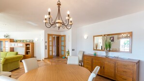 Un coin repas comprenant une table ronde en bois, des chaises blanches, un buffet en bois et un lustre.