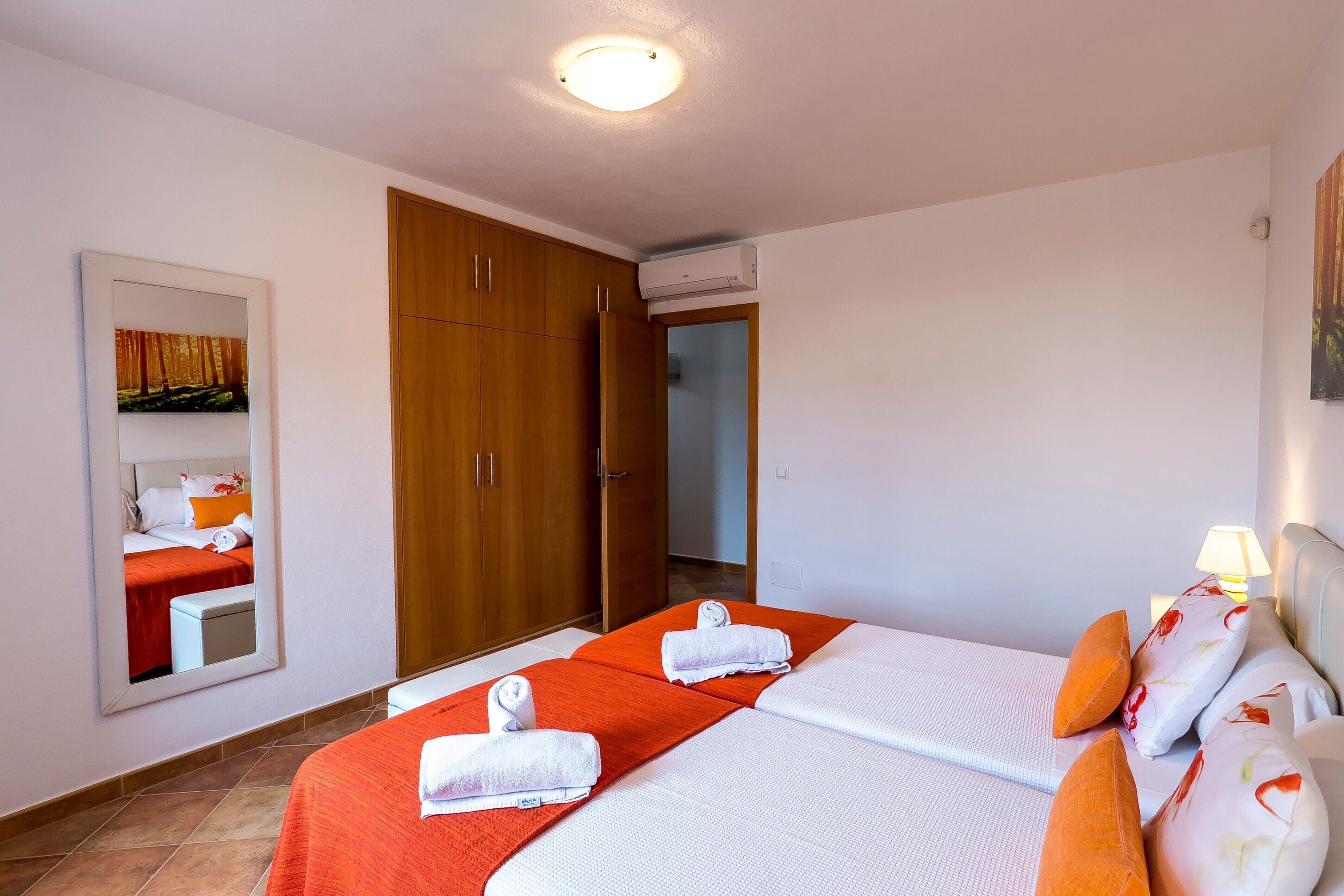 A hotel room with two beds, a wooden wardrobe, a mirror, and a ceiling light.