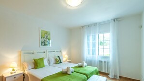Une chambre d’hôtel avec deux lits, une table de chevet avec une lampe, une fenêtre avec des rideaux et un radiateur.