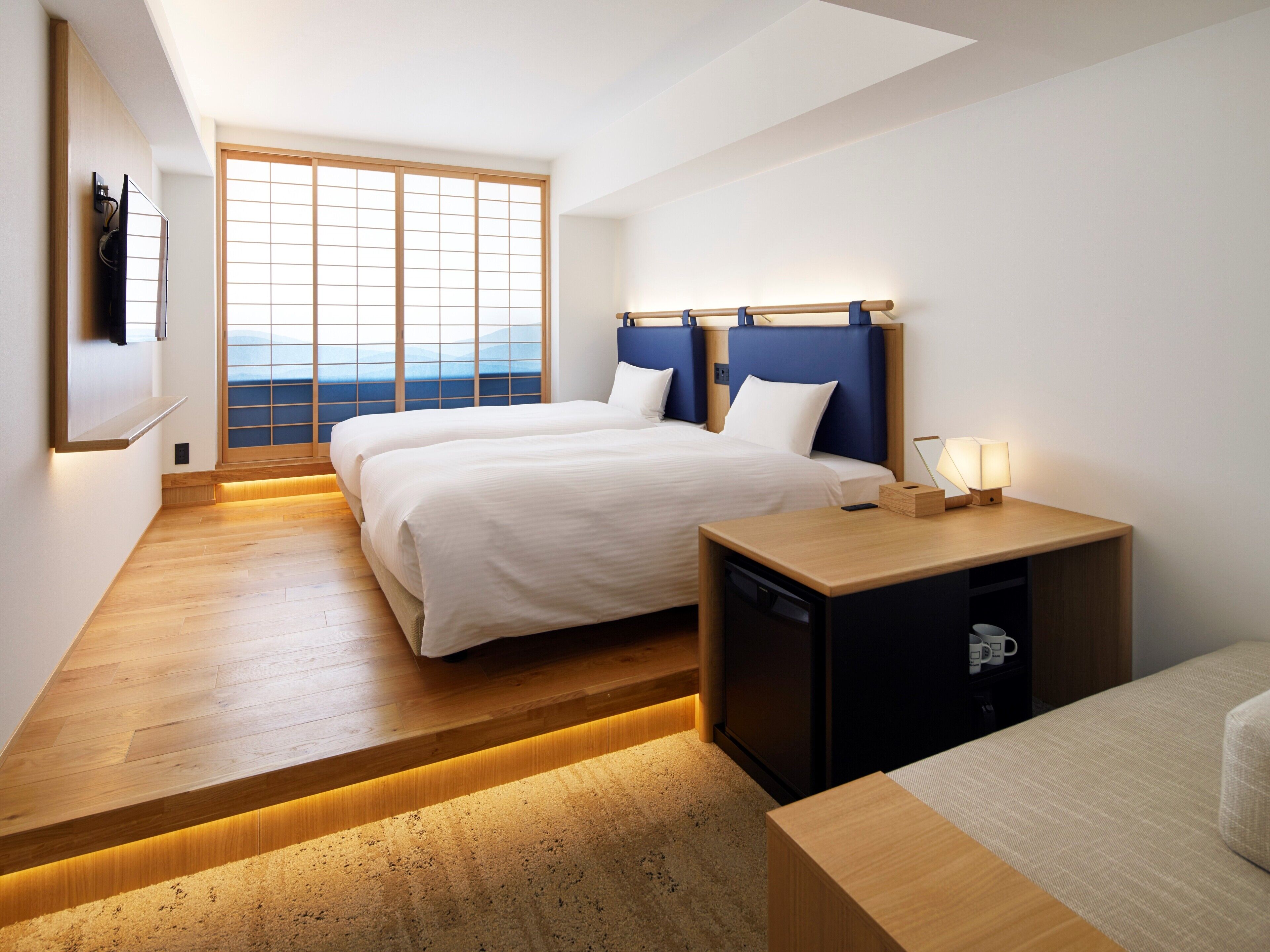 Une chambre d’hôtel avec deux lits, un bureau et une vue sur l’océan grâce à de grandes fenêtres.