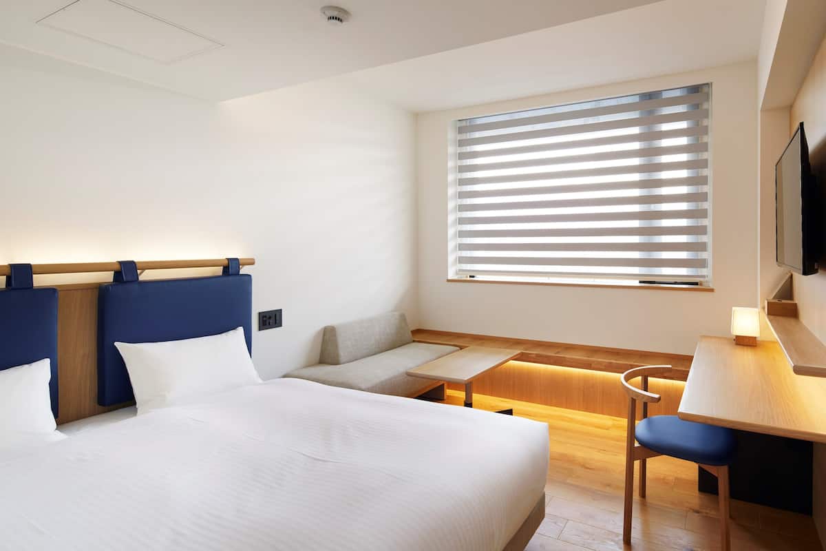 Une chambre d’hôtel moderne équipée d’un grand lit, d’un bureau, d’une chaise et d’une fenêtre avec des stores.
