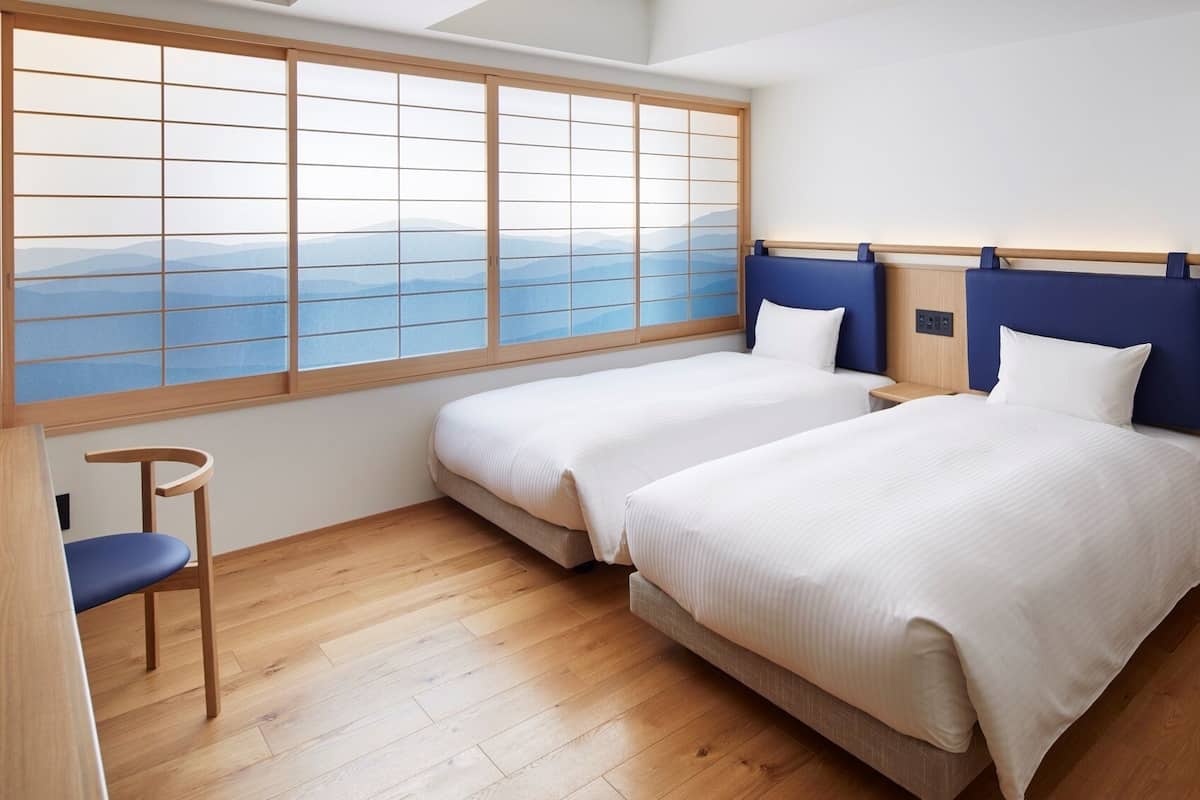 Une chambre d’hôtel avec deux lits, un bureau, une chaise et une grande fenêtre donnant sur les montagnes.