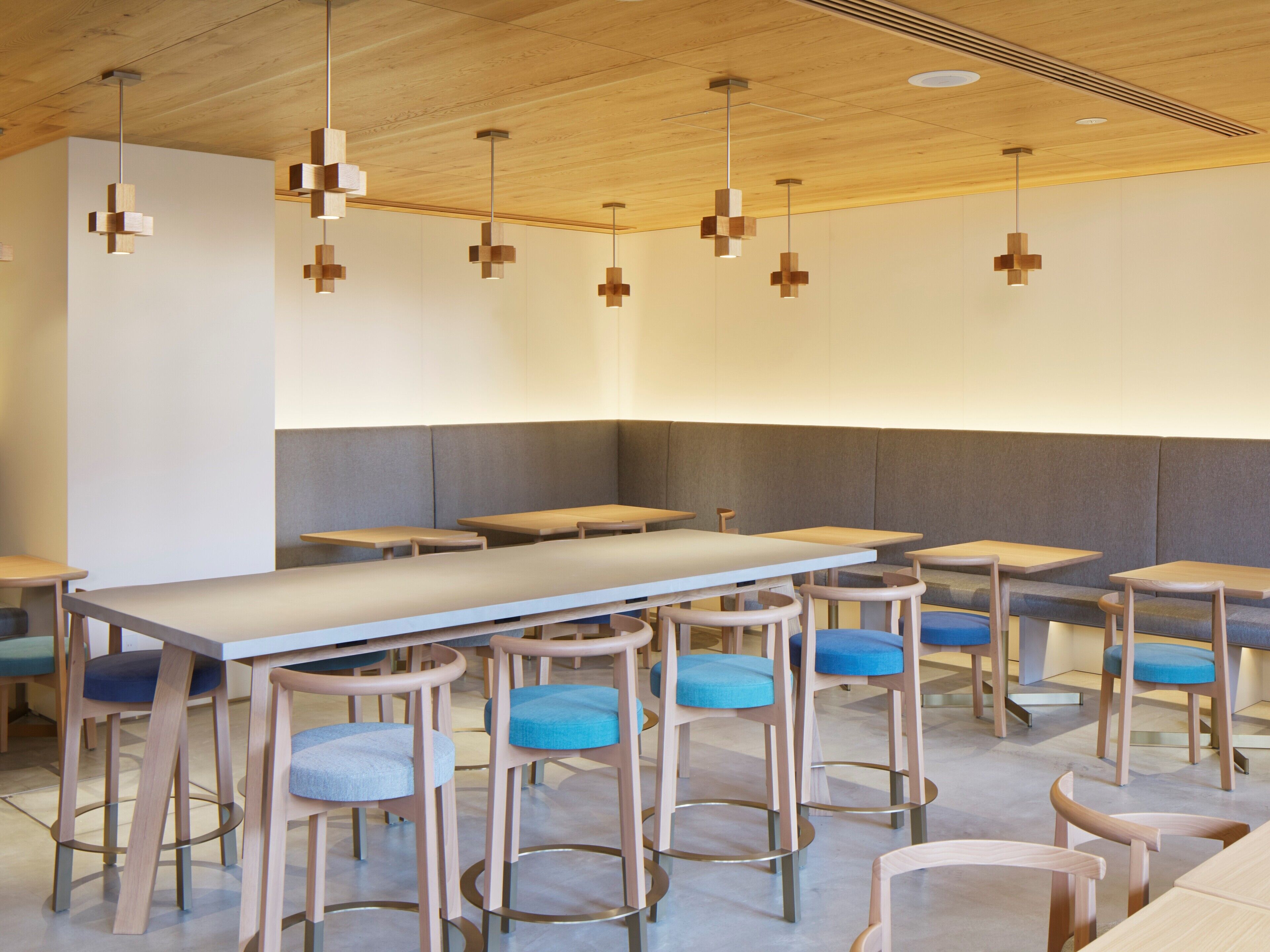 A modern restaurant interior with wooden ceiling, white tables, and blue cushioned chairs.