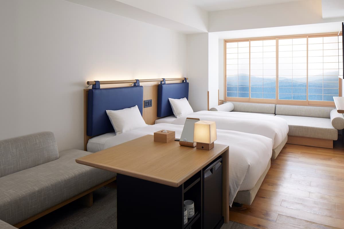 Une chambre d’hôtel avec deux lits, un canapé, un bureau et une grande fenêtre donnant sur un beau paysage.