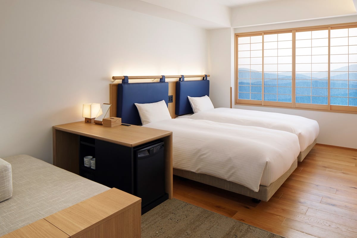 Une chambre d’hôtel avec deux lits, un bureau et une fenêtre donnant sur la montagne.
