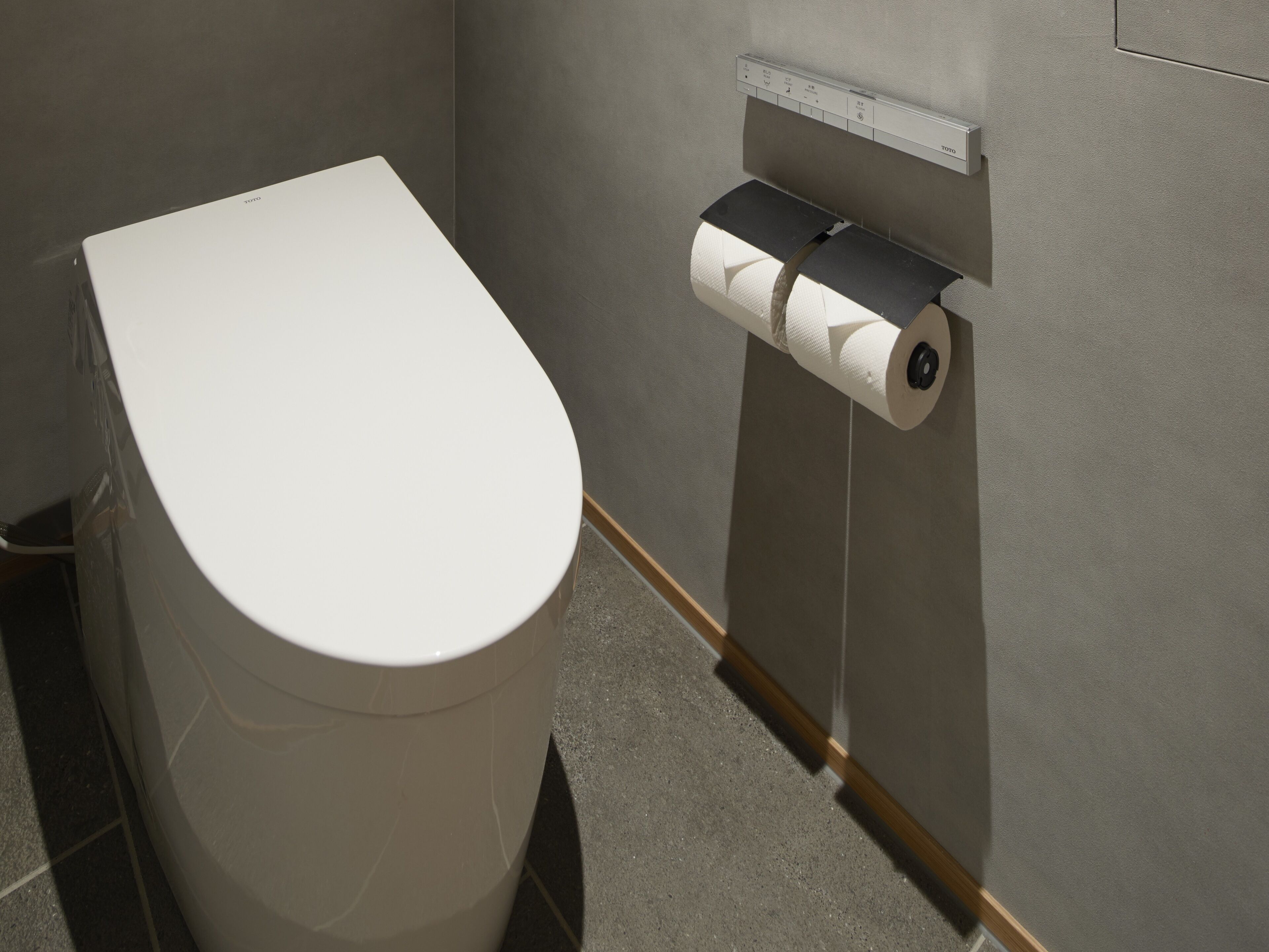 Des toilettes avec un porte-rouleau de papier toilette fixé au mur.