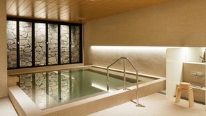 Wellnessbereich mit einem gläsernen Whirlpool, Steinwand, Holzboden und einem kleinen Holzschemel.