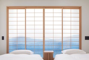 A room with two beds, a wooden floor, and a view of mountains through a shoji screen.