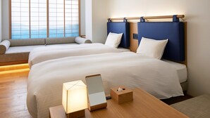 Ein Hotelzimmer mit zwei Betten, einem Nachttisch aus Holz, einer kleinen Sitzecke und einem Fenster mit Blick.
