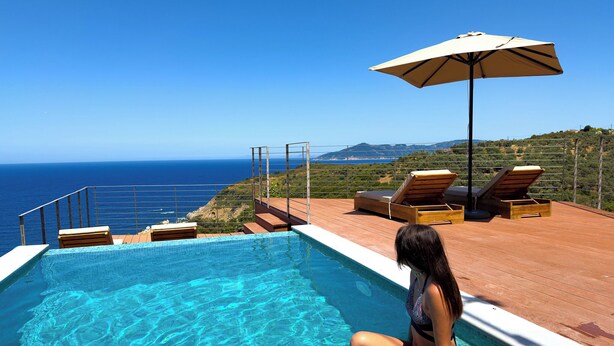 A pool with clear water, a woman sitting by the pool, and a view of the ocean.