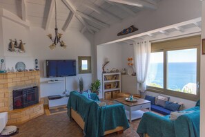 Een woonkamer met een open haard, bank, salontafel en uitzicht op zee.
